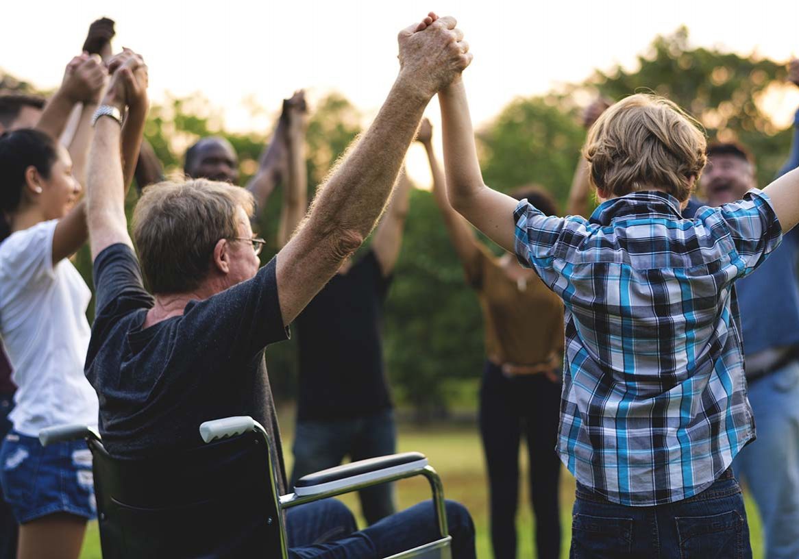 A diverse group of people, including a man using a wheelchair, joining raised hands together outdoors