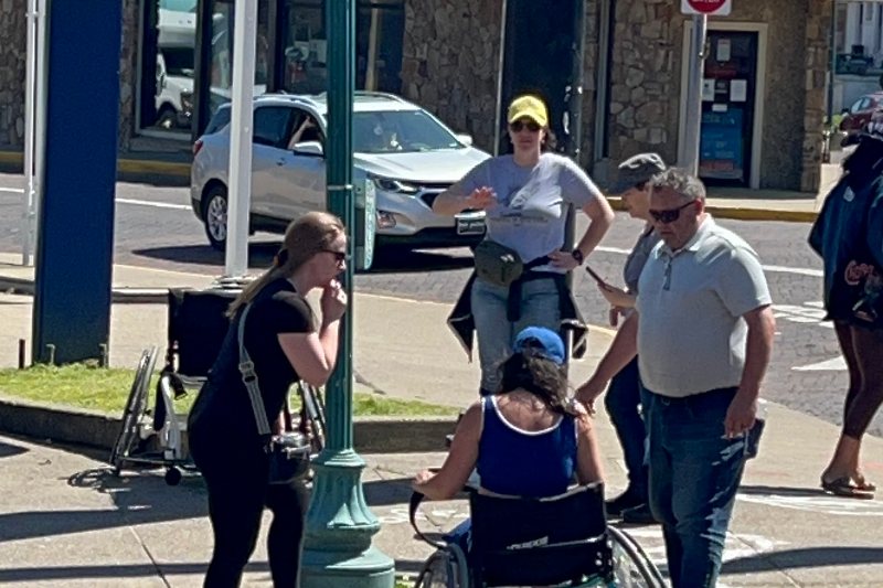 SOCIL staff and community members check a curb cut with a woman using a manual wheelchair at a downtown intersection