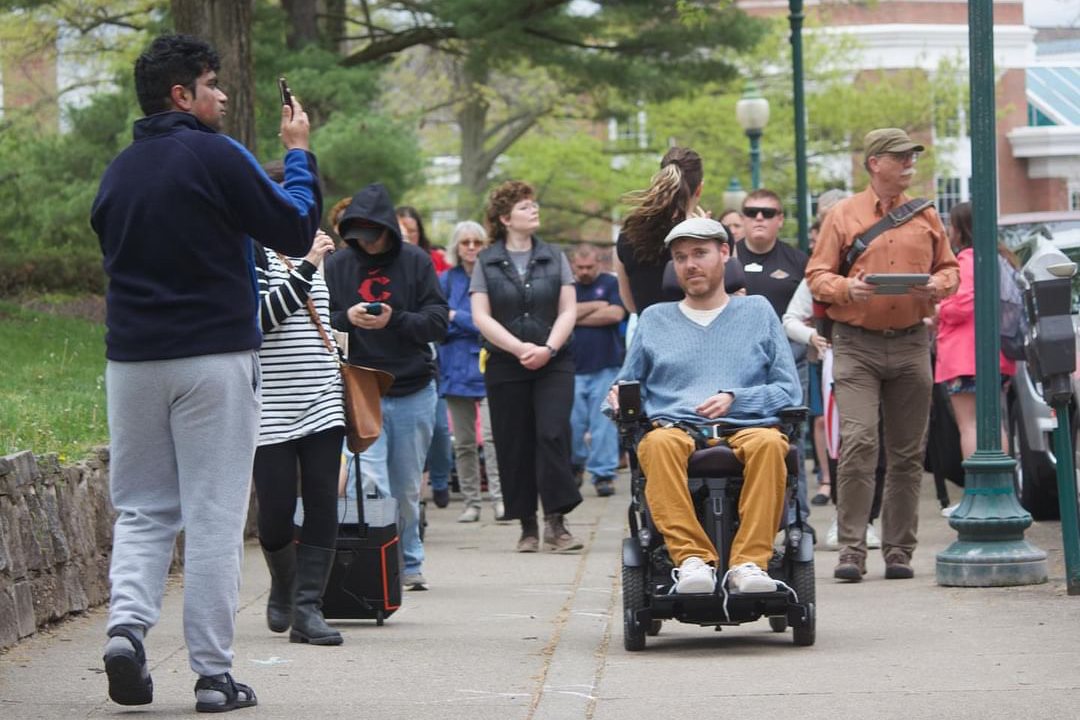 Community members walk with a man in a power wheelchair during an accessibility walk in downtown Athens