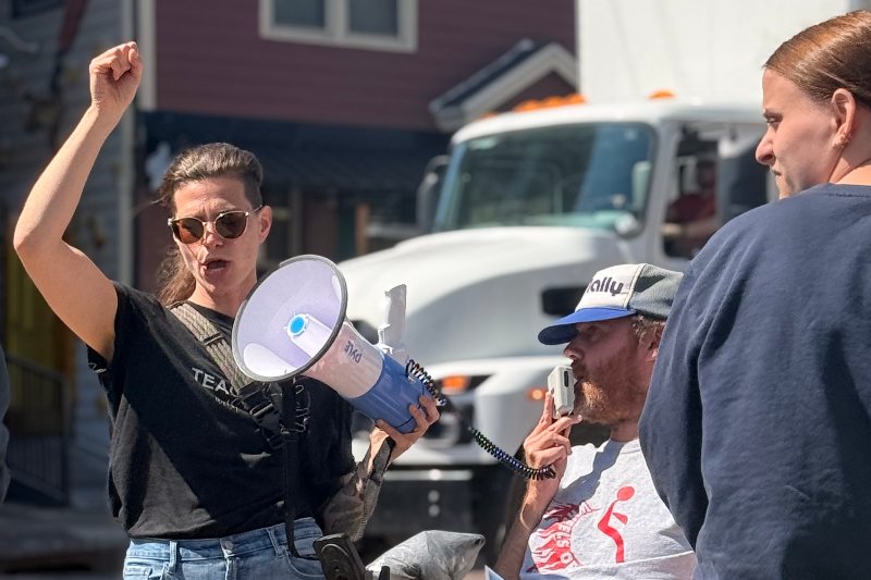 An advocate raises her fist and speaks through a megaphone with a man in a power wheelchair at an accessibility rally