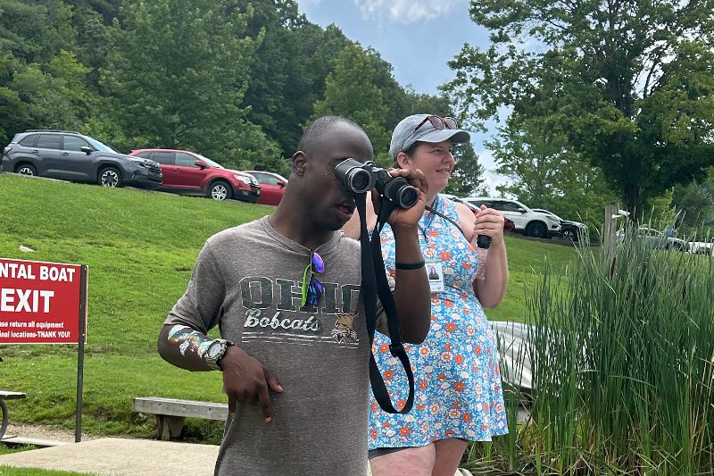 A participant looks through binoculars with a SOCIL staff member during a lakeside outing